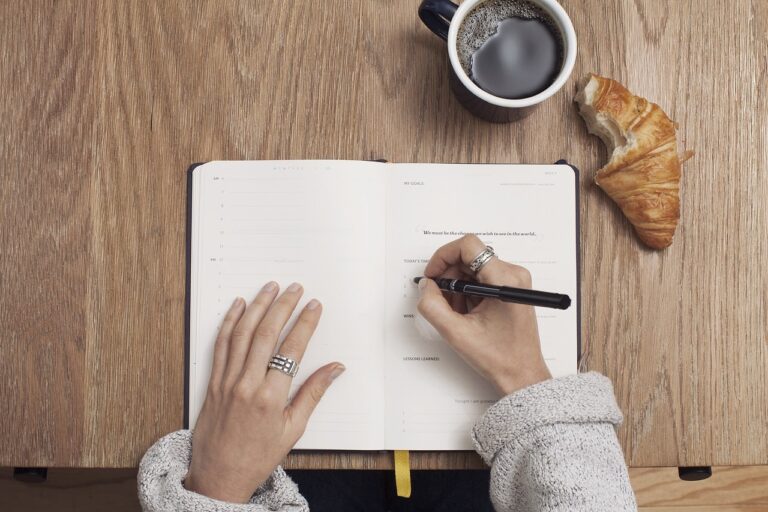 table with americano and crosisant, with someone writing in a journal